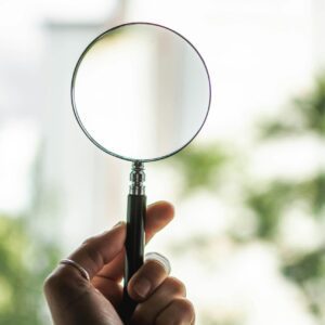 Close-up of a hand holding a magnifying glass on a sunny day outdoors.