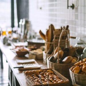 Side view of delicious fresh baked baguette and buns in wicker basket and fresh baked pies and croissant in bakery in daytime