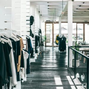 Interior of spacious modern fashion boutique with collection of various clothes hanging on racks in sunlight